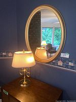 View of the oval mirror on the wall above a wooden table with the vintage brass trumpet table lamp lit in front.