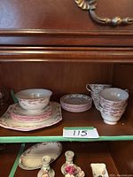 Shelley fine bone china teacups, plates, saucers, and bowl with floral pink rose pattern on wooden shelf inside cabinet.
