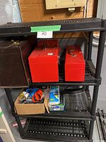 Full view of black plastic shelving unit with two red metal tool boxes, a brown leather tool bag, and small tools and supplies on shelves