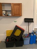 Photo showing two black storage bins filled with various hand tools, lids or panels with red edges leaning on them, and bright yellow panels behind.