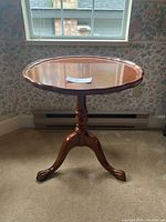 Front view of the vintage wooden side table showing round scalloped edge top and tripod claw foot base.