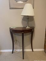 Full view of vintage half moon console table with lamp on top against a wall showing the overall condition and style.