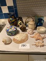 Multiple vintage and nautical decor items arranged on a counter including ceramic vases, shells, and a tin box.