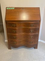Front view of vintage wooden secretary desk showing four front drawers and slant-front top closed.