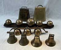 Photo showing the entire collection of bells laid out with two large cowbells in the back, two sets of sleighbells on metal strips in the middle, and four smaller livestock bells in front. Green apple used for scale is not included in the lot.