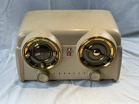 Front view of the cream-colored Crossley D-25 radio showing twin dials with gold accents and control knobs.