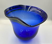 Front angled photo showing the shape, color, and signature of the hand blown blue vase with wavy rim and stripe details.