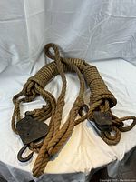 Photo of coiled vintage nautical rope hoist with two metal pulleys and hooks resting on white cloth background, natural fiber rope, rusty metal parts