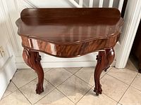 Full front view of the mahogany console table with curved edges and carved legs.