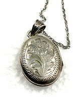 Close-up showing the floral engraving detail on the silver oval locket pendant.