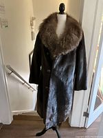 Front view of full-length black mink coat on mannequin, showing three-button closure and brown collar.