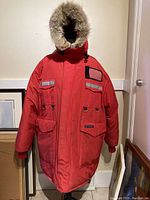 Front view of red parka on mannequin showing hood, fur trim, front pockets