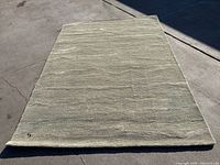 Full view of green 5'x7' carpet on pavement, showing shape and overall color with slight shadowing