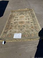 Full photo showing the 5x8 size rug laid out flat on a concrete surface with a paper indicating size.