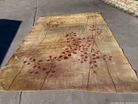 Full view of the beige carpet with red leaf and brown branch design laid flat on concrete outdoors.