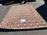 Full view of the 8'x11' beige Turkish rug with red geometric diamond pattern on a sunny outdoor surface, with a paper label showing dimensions on top.