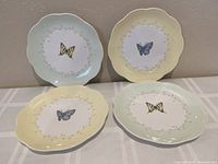 Four Lenox Butterfly Meadow dessert plates arranged in two rows, alternating between yellow and green borders with butterflies.