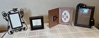 Four decorative picture frames arranged: black metal frame with scrollwork, small dark wood rectangular frame, oval Mickey Mouse frame with pin inside, and square wood frame with etched bird artwork.