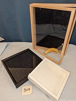 Large taupe display case standing upright with two smaller black and white shadow boxes lying in front. Banana included for scale.