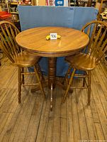 Full view of three-piece wooden bistro set with round table and two chairs in wood finish on wood floor.
