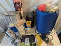 Full view of assortment including cooler, mugs, sleeping bag, lantern, books, survival kit, and coffee maker.