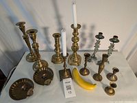 All 13 pieces displayed on a white surface including two tall matching candlesticks, two matching wall sconces, and seven assorted brass candlesticks with a banana for scale.