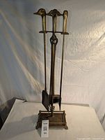 Full view of brass fireplace tool set with stand and four tools.