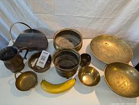 Photo showing full lot of 10 brass items with banana for scale. Several bowls, planters, and pots visible.