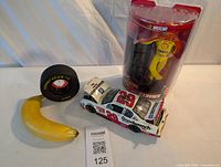 Photo showing diecast car, Goodyear ashtray, Kevin Harvick action figure in packaging, and banana for scale