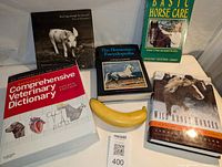 Five animal related books arranged with a banana for scale. Titles from left to right: Comprehensive Veterinary Dictionary 4th Edition, a photo book with black and white pig cover, The Horseman's Encyclopedia, Basic Horse Care, Wild About Horses.