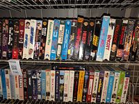 Photo showing two shelves filled with VHS tapes, displaying colorful spines with various movie and entertainment titles showing the large collection available in the lot.