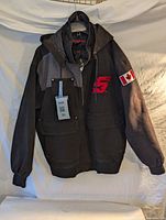 Front view of black and dark grey men's winter jacket with zipper and snap pockets, Snap-On logo on chest, and Canadian flag patch on left sleeve.