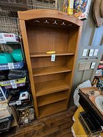 Front view of the wooden pantry shelf unit showing five shelves and the curved top with a metal stemware rack above the top shelf.