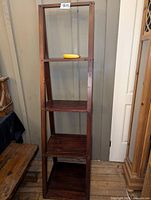 Front view of the ladder shelf showing four wooden shelves with a dark polished finish and tapered design.