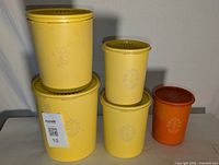 Front view of 4 stacked yellow Tupperware containers with 1 small orange container placed beside them on a white surface.