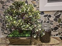 Artificial bonsai plant with green leaves and LED lights in a rectangular metallic planter, next to a glass jar filled with coffee beans.