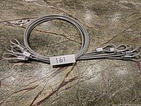 Photo showing five coiled stainless steel spring wires with PVC coating and looped ends, lying on a stone surface with the label '161'.