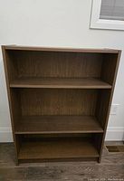 Front view of the three-shelf brown walnut effect bookcase showing clean interior and sturdy build.