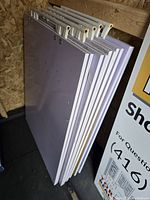 Stack of five white-sided signs with protective cellophane wrap visible on edges, stored in a garden shed area.