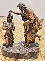 Front view of the bronze statue showing detailed figures of John the Baptist baptizing Jesus Christ, highlighting the water pouring action and textured base.