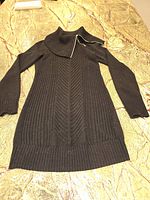 Front view of the black long ribbed knit sweater jacket laid flat on a stone surface showcasing its full length and collar detail.