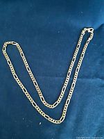 Full view of the chain link necklace laid out on a blue fabric background showing the full length and link style.