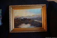 Full view of antique oil painting in ornate gesso frame with a sunset and cows near water and mountains