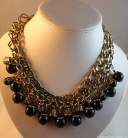 Front view of double bib style necklace with two gold-tone chains and black beads encased in decorative caps, displayed on mannequin bust.