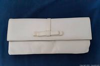 Front view of white leather clutch bag displaying flap closure and long leather strap with bow detail