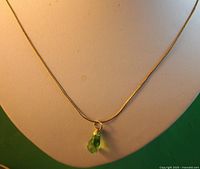 Full view of the necklace showing the gold-colored chain and the green glass teardrop pendant.