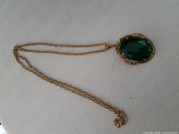 Full view of gold-tone chain necklace with large green glass stone pendant lying on fabric background