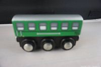 Top side view of the green wooden passenger box car with detailed window illustrations and three silver axled wheels.
