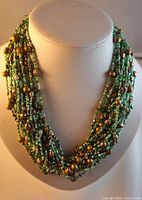 Front view of the multi strand necklace showing green and taupe beads on a mannequin bust.