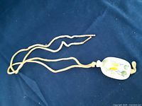 Porcelain potion jug pendant necklace laid on a dark blue fabric background, showing the full pendant and beige cord with knot closure.